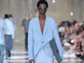 Modello con outfit uomo elegante senza giacca, completo azzurro, occhiali da sole blu e borsa a righe.