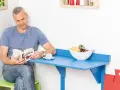 Mann liest Buch an selbstgebautem Klapptisch. Obstschale und Kaffeetasse stehen bereit.
