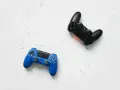 Dos mandos de videojuego, uno azul y otro negro, listos para una intensa sesión de videojuego de acción y aventura.