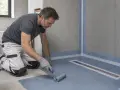 Operaio applica uno strato di impermeabilizzazioni edili con un rullo, preparando una doccia a filo pavimento.
