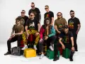 Grupa mężczyzn w koszulkach z motywami nawiązującymi do rastafarianizmu. Jeden z nich ma dredy i kolorową kurtkę, co może kojarzyć się z tym, czym jest rastafarianizm.