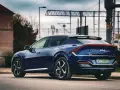 Granatowe Kia EV6 GT z charakterystycznym pasem świateł z tyłu, zaparkowane przy drodze z widoczną infrastrukturą kolejową.