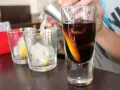 Jak pić sambucę? W szklance ciemny likier z plasterkiem pomarańczy i lodem. Obok szklanki z lodem i cytryną.