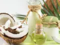 Aceite de coco para el pelo en frascos y botellas, junto a cocos frescos y hojas verdes.