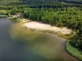 Piękny, piaszczysty brzeg nad zbiornikiem Pogoria, otoczony zielonym lasem. W oddali widać budynek z pomostem i łódkami.