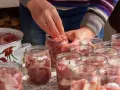Ręce wkładają kawałki mięsa do słoików, przygotowując domowy gulasz angielski. Obok stoi garnek z pokrojonym mięsem.