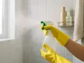 Yellow-gloved hands spray cleaner onto white tile, demonstrating how to clean a tile shower.