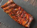 Costillas a la miel, glaseadas y jugosas, servidas sobre una pizarra oscura.