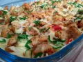 Pyszna zapiekanka gyros z makaronem, posypana serem i natką pietruszki, w szklanym naczyniu.