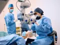 Chirurghi in sala operatoria, uno esegue una vitrectomia non riuscita con un microscopio, mentre un altro assiste.