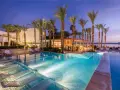 Luxury resort pool with palm trees and lounge chairs at dusk.