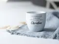 Weiße Tasse mit dem Schriftzug "Ich vermag alles durch den, der mich stark macht, Christus. Philipper 4,13" auf einem grauen Stoff.