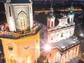 Wieża trynitarska nocą, z ludźmi na balkonie i oświetloną fasadą kościoła.