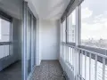 Zabudowa balkonu w bloku z widokiem na miasto. Szklane drzwi i okna tworzą przestronne wnętrze.