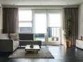 Nowoczesny salon z szarą kanapą, stolikiem i dużym oknem z roletami.