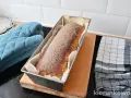 Świeżo upieczony chleb cebulowy na zakwasie w keksówce, gotowy do wyjęcia. Obok rękawica kuchenna i ściereczka.