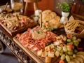 Stół z przekąskami: wędliny, sery, owoce, pieczywo i paluszki.