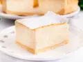 Puszysty sernik z mascarpone, oprószony cukrem pudrem, na białym talerzyku. Idealny na deser.