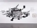 Œuvres d'Abdelkader Benchamma : une explosion d'encre noire sur mur blanc, encadrée par des dessins et peintures.