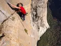 Ein Mann klettert free solo eine steile Felswand empor, mit einem tiefen Abgrund unter ihm.