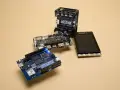 An Arduino Uno, a Bela GEN MULTI, and a Fruit Jam RP2350 board are arranged on a beige surface, showcasing some of the best microcontroller options for makers.