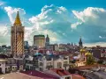Widok na stolicę Adżarii, Batumi, z charakterystyczną wieżą zegarową i złotymi kopułami cerkwi pod błękitnym, chmurowym niebem.