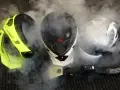 Pulizia del casco con vapore. Tre caschi, uno giallo fluo, uno bianco e nero, uno bianco e nero con visiera, circondati da fumo.
