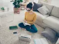 Dziewczyna w okularach uczy się w domu, przygotowując się do egzaminów licealnych. Na dywanie ma laptopa, książki i notatnik.
