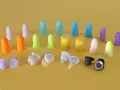 Apprenez comment mettre des bouchons d'oreilles en mousse. Divers bouchons colorés et écouteurs sans fil sont disposés sur fond jaune.