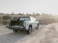 Biały maxus pickup z otwartą paką stoi na żwirowej drodze przy zbiorniku wodnym.
