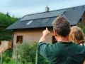Ojciec z dzieckiem patrzą na dom z panelami fotowoltaicznymi. Zastanawiają się, fotowoltaika 6 kw ile wyprodukuje energii.