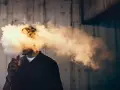 Hombre exhalando una gran nube de humo vaper, que envuelve su cabeza.