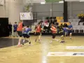 Kacper Wachowiak w akcji podczas meczu piłki ręcznej. Zawodnicy w czerwonych i niebieskich strojach walczą o piłkę na parkiecie.