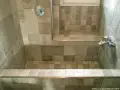 Bagno con vasca da bagno in muratura fai da te, rivestita con piastrelle grigie di varie tonalità e fantasie.
