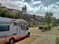 Camper in sosta a Belluno, con case colorate e un campanile sullo sfondo.
