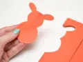 En hand håller en orange pappersfigur av en påskhare.