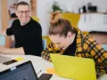 Zwei lachende Kollegen am Schreibtisch mit Laptops. Ein bezahltes Auslandspraktikum kann so Spaß machen!