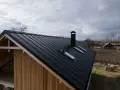 Montaż podbitki stelaż na dachu z blachy. Widok na dom z drewnianą elewacją i kominem.