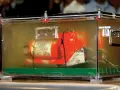 Pomarańczowa skrzynka "czarnej skrzynki" z napisem "FLIGHT RECORDER DO NOT OPEN" w przezroczystej obudowie, dowód w sprawie wypadku lotniczego.