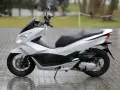 Biały skuter Honda PCX na mokrym bruku. Zastanawiasz się, od ilu lat można jeździć skuterem 50? Od 14 roku życia z kartą motorowerową.
