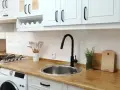 Cocina renovada: gabinetes blancos, encimera de madera y grifo negro. ¡Un ejemplo de cómo pintar muebles de melamina para darles nueva vida!