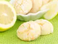 Biscotti al limone spolverati di zucchero a velo, accanto a fette di limone fresco su sfondo verde.