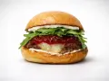 Soczysty burger z rukolą, konfiturą i roztopionym serem na białym tle.