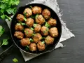 Polpette al forno dorate e succulente, guarnite con prezzemolo fresco, in una padella di ghisa su sfondo scuro.