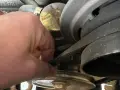 Hand prüft Keilriemen, der beim Anfahren quietscht. Der Riemen läuft über mehrere Riemenscheiben im Motorraum.