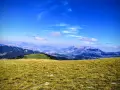 Prato verdeggiante con vista panoramica sul monte Pizzalto e le montagne circostanti sotto un cielo azzurro con nuvole sparse.