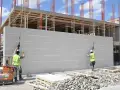 Chantier de construction : deux ouvriers installent un mur en siporex extérieur. Le bâtiment en cours de construction est visible en arrière-plan.