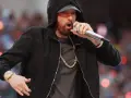 Eminem w czarnej bluzie z kapturem śpiewa do mikrofonu, w złotym łańcuchu i zegarku.