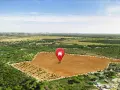 Terreno llano y despejado, marcado con un pin de casa, rodeado de pinos y vegetación. Un área de suelo terciario ideal para construir.