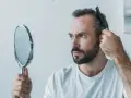 Mann kämmt sich die Haare, besorgt über Haarausfall. Er fragt sich, warum seine Haare nicht mehr wachsen, Frau.
